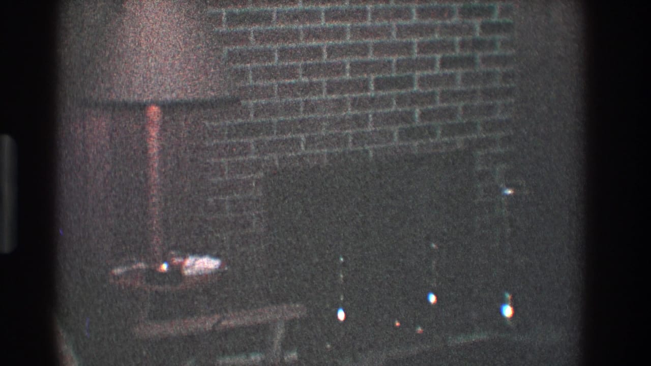 Dim living room with brick fireplace, floor lamp, small table, and dark hearth.
