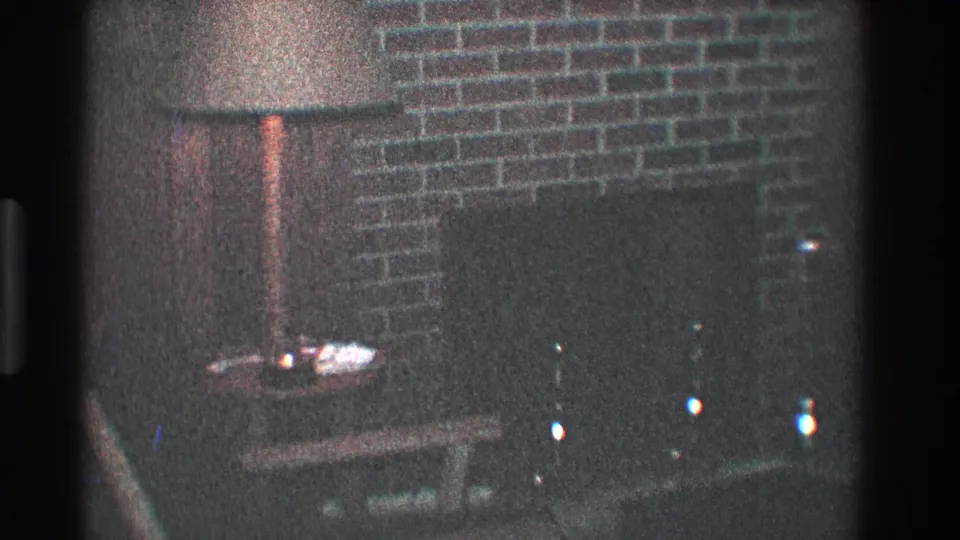 1968 Toledo interior frame with a floor lamp, brick fireplace wall, dark hearth area, and small table in soft focus.