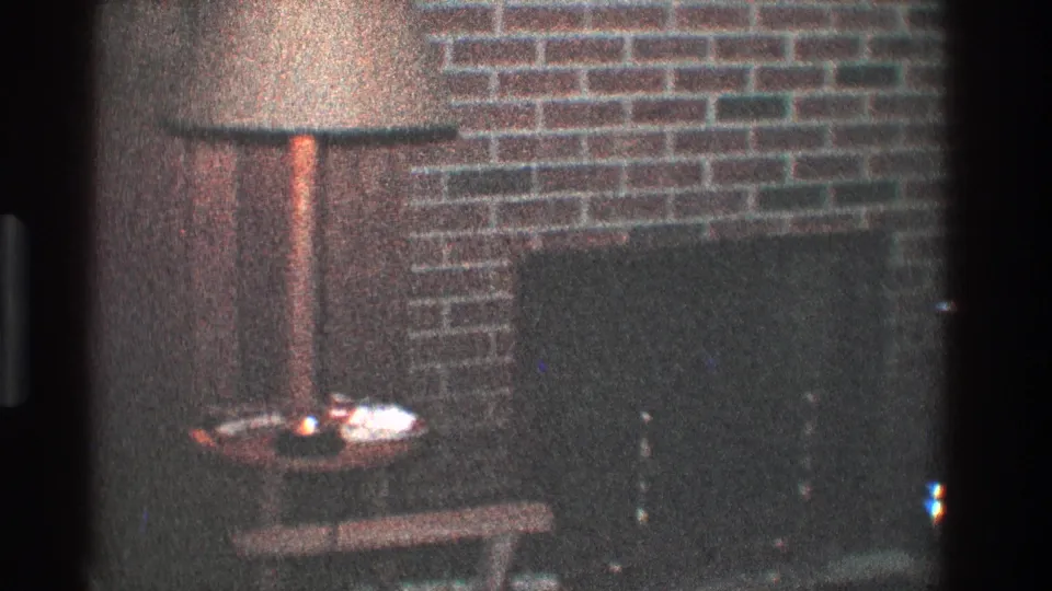 1968 Toledo home interior frame showing a closer view of the lamp, brick fireplace wall, dark hearth, and small table.