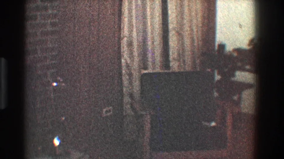 1968 Toledo home-movie frame showing a dim living room with brick fireplace, armchair, and heavy curtains before the camera reaches the television.