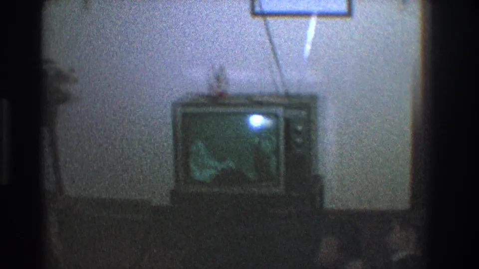 1968 Toledo frame centered on an old tube television with rabbit-ear antenna, glowing blue screen, framed wall decor, and a small figurine on top.
