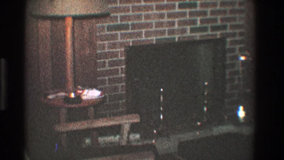 1968 Toledo living-room frame showing a brick fireplace, dark hearth screen, side table with a small light or candle, and a wooden bench.