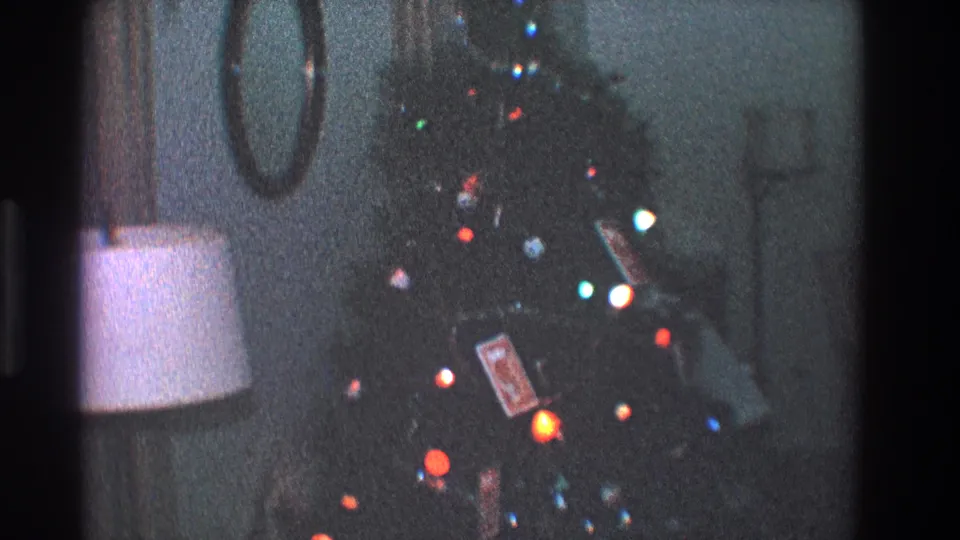Grainy 1968 Toledo frame showing a holiday tree with red, blue, green, and orange lights in a private living room.