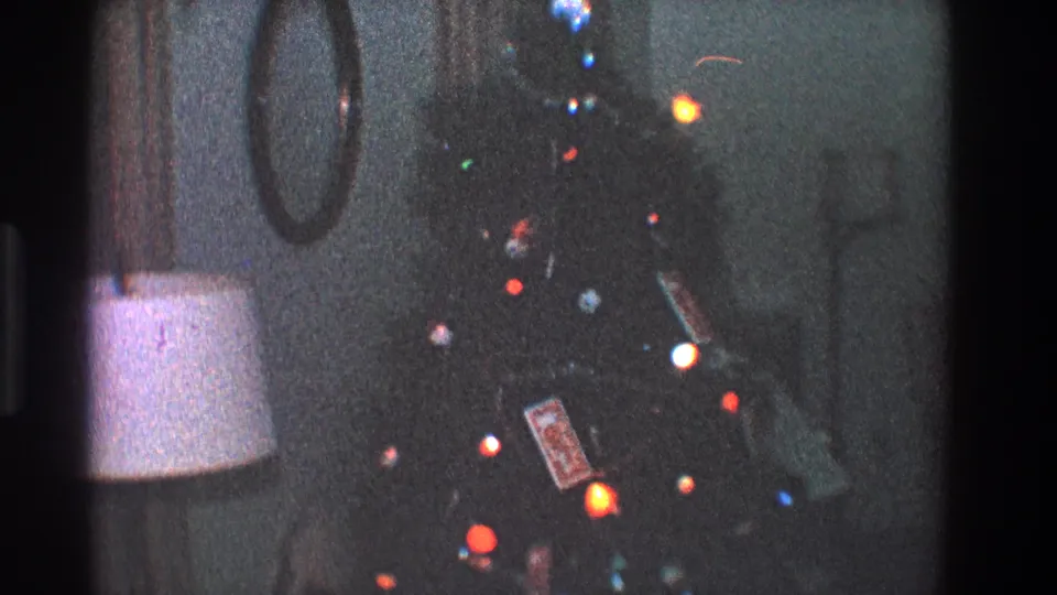 Late-1960s Toledo home-movie frame of a decorated Christmas tree with glowing bulbs, ornaments, and nearby room furnishings.