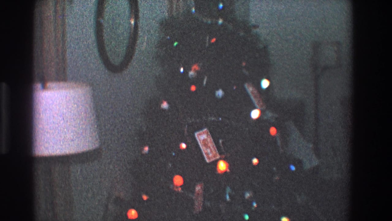Christmas tree with colored lights and ornaments near a lamp in a dark room.