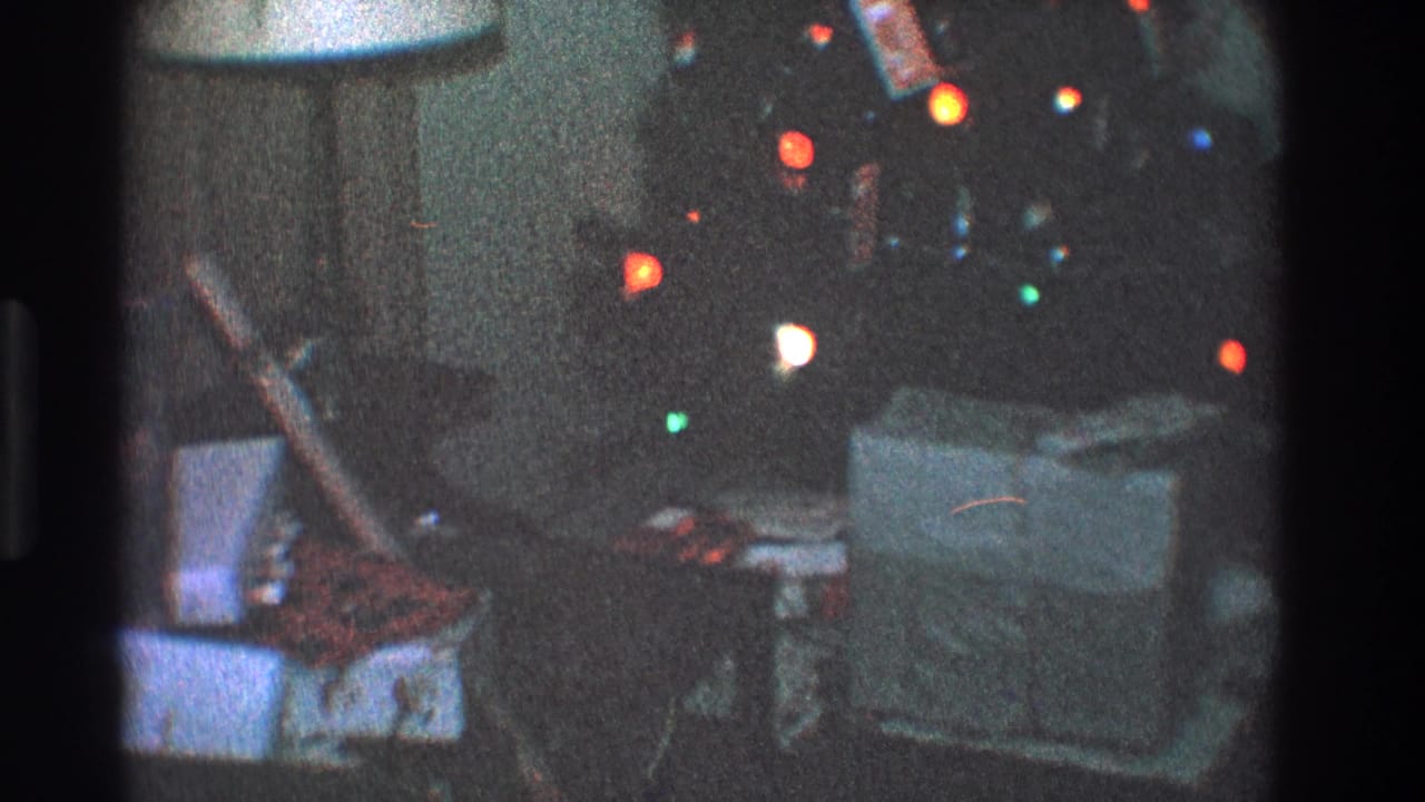 Wrapped presents on a couch beside a lit Christmas tree in a dim living room.