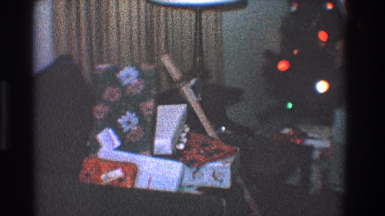 Gift boxes and floral decor on a couch with Christmas tree lights behind them.
