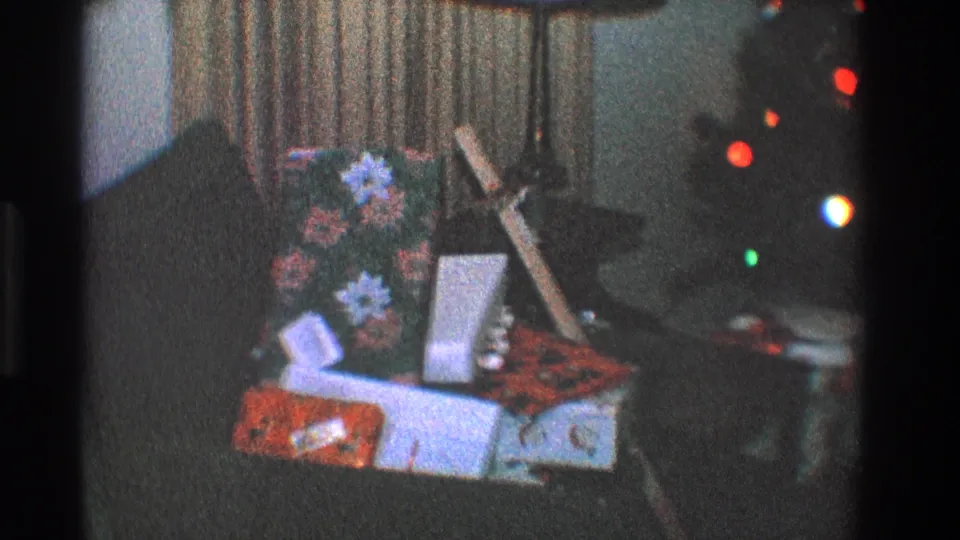 1968 Toledo home interior showing stacked Christmas presents, flowers, curtains, and glowing tree lights in low 8mm exposure.