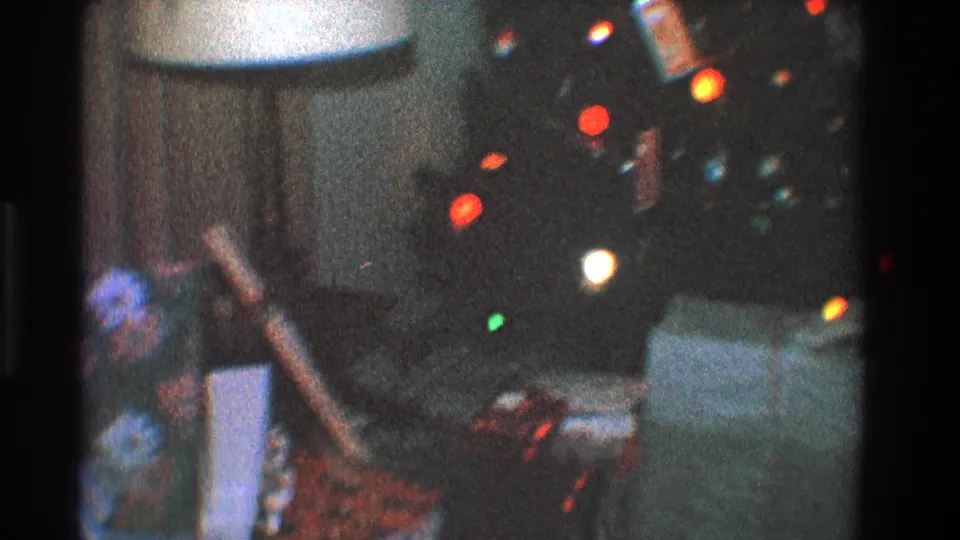 1968 Toledo 8mm frame with colored Christmas lights, wrapped gifts, a couch, and a lampshade in a private living room.
