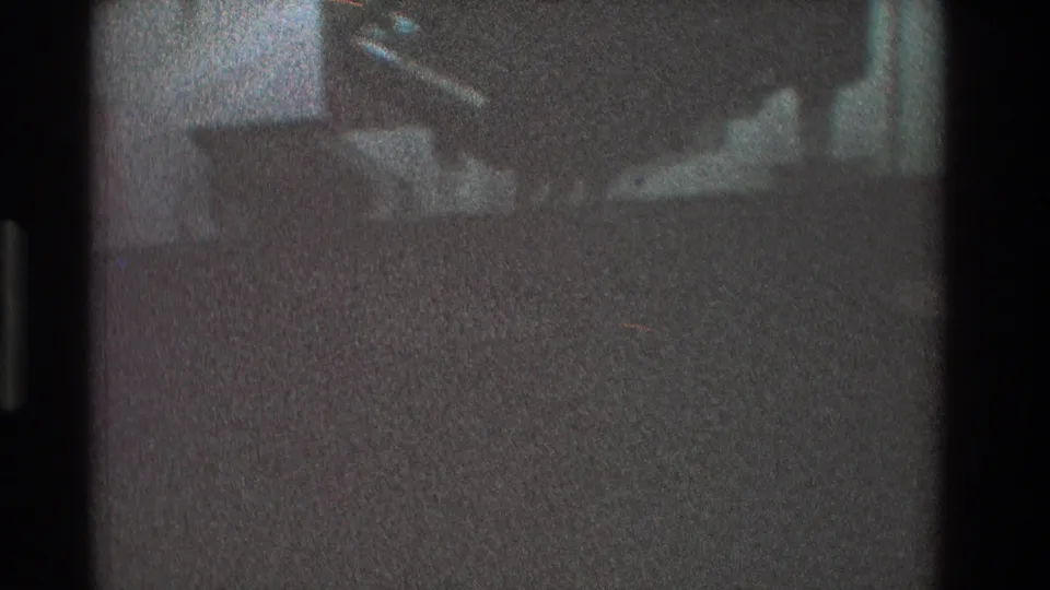 Soft, underexposed 1968 Toledo interior frame showing dark carpet and part of a vintage chair in a private living room.