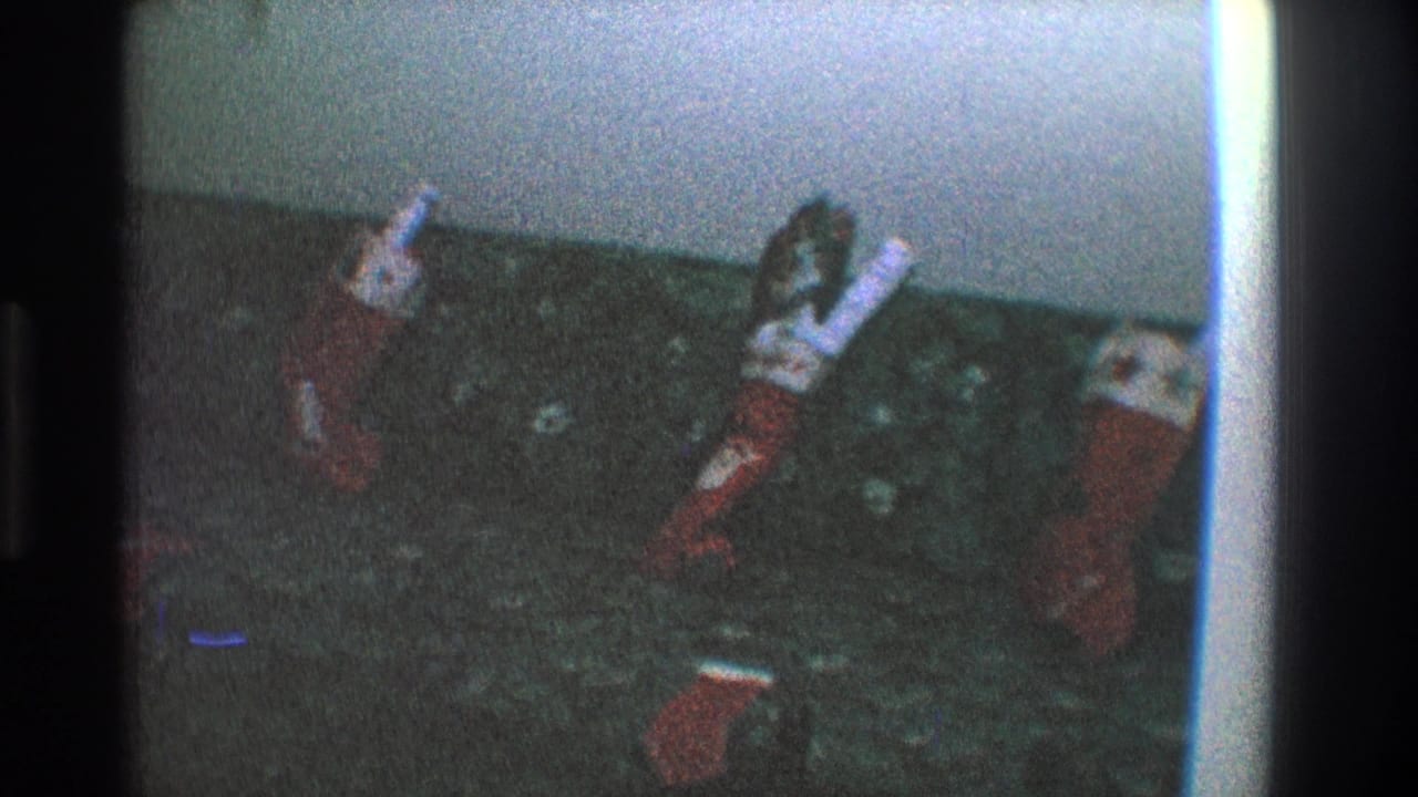 1968 Toledo home-movie frame showing stuffed red-and-white Christmas stockings arranged on a dark patterned couch.