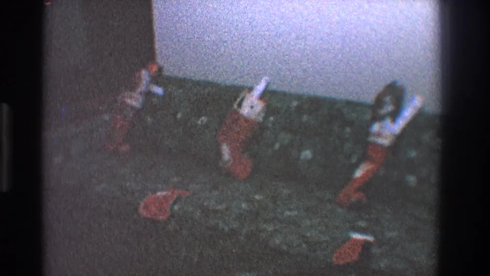 1968 Toledo home-movie frame with stuffed Christmas stockings spread across a dark couch in low interior light.