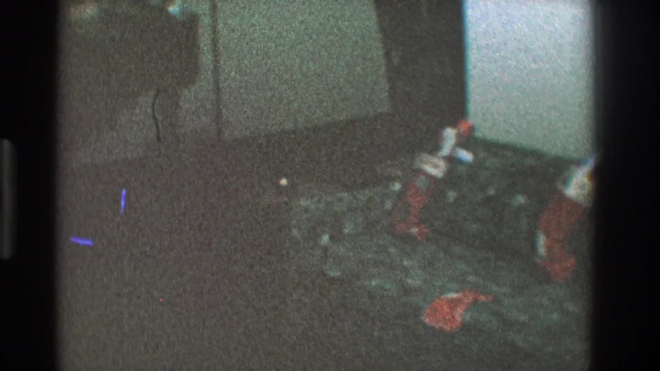 1968 Toledo home-movie frame showing stockings along a couch near a wall corner in a dim living room.