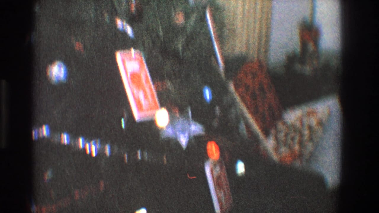 Soft 8mm view of Christmas tree lights and wrapped presents in a dim room.