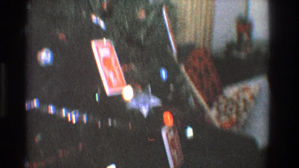 1968 Toledo home-movie frame showing glowing tree lights, ornaments, and wrapped gifts in a dim Christmas interior.