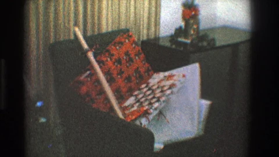 1968 Toledo Christmas frame focusing on a red patterned blanket or textile, white box, curtains, and dark couch in a private interior.