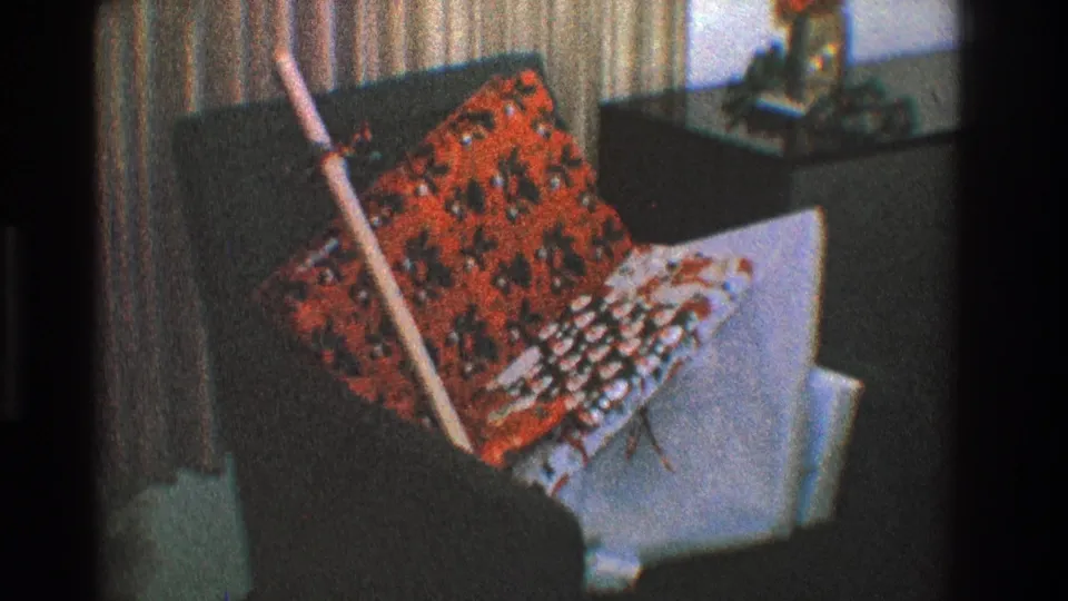 1968 Toledo home interior showing a lounge chair with patterned pillows and a broom leaning in front of striped curtains.