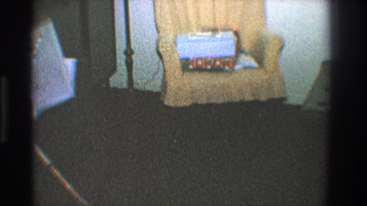 Upholstered chair with a wrapped gift box on the seat beside a dark carpeted floor.