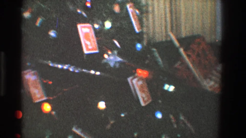 1968 Toledo home-movie frame of a lit Christmas tree with ornaments, tinsel, gifts, and a radiator in a private living room.