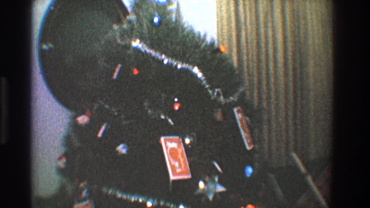 Decorated Christmas tree seen closer with tinsel, colored bulbs, and cards hanging as ornaments.