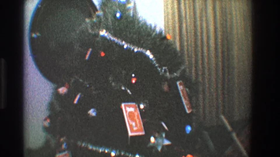 Close 8mm view of a Toledo Christmas tree with tinsel garland, colored lights, and playing cards used as ornaments.