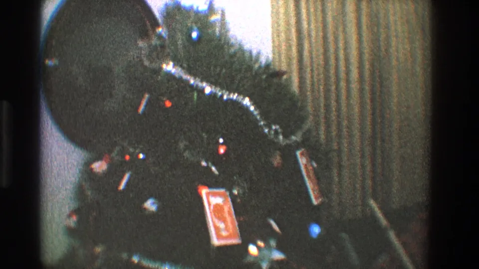1968 home-movie frame from Toledo showing a decorated tree with glowing bulbs, tinsel, and a red playing-card ornament.