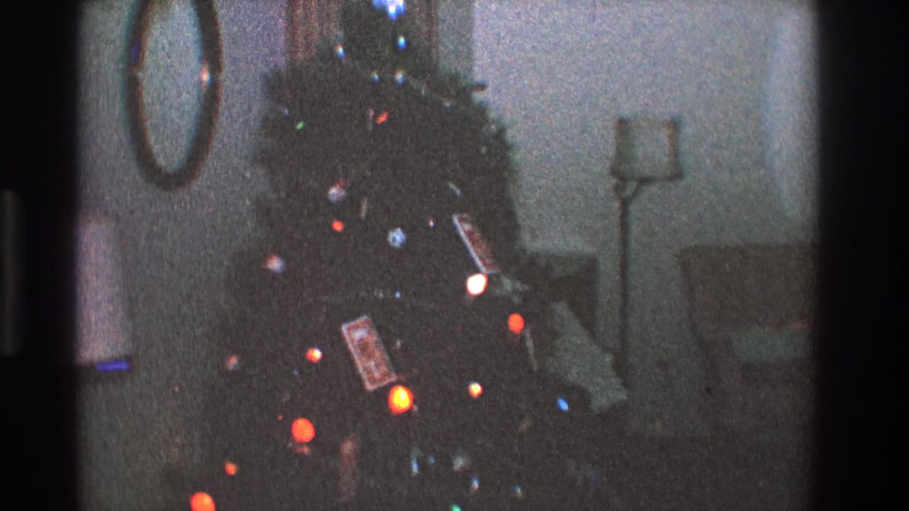 Decorated Christmas tree with glowing bulbs, ornaments, wrapped gifts, and furniture in the background.