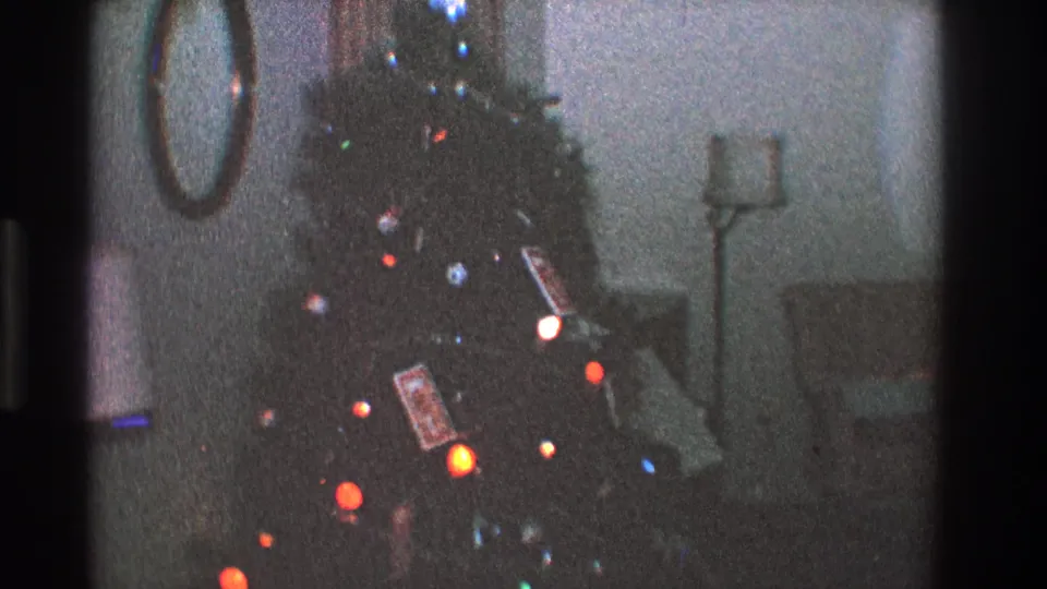 1968 Toledo interior view of a Christmas tree with glowing multicolored bulbs, ornaments, wrapped gifts, and soft-focus room furnishings.