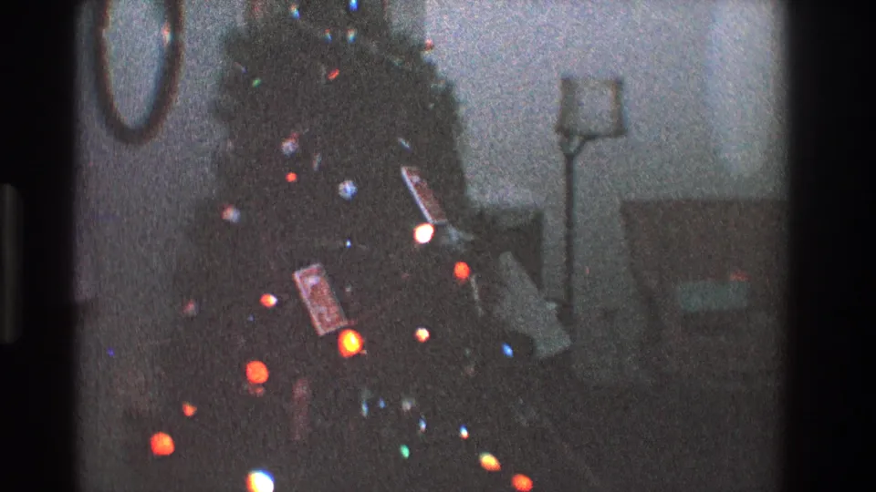 1968 Toledo 8mm frame of a Christmas tree with colored lights, hanging ornaments, wrapped gifts, and a round mirror on the wall.
