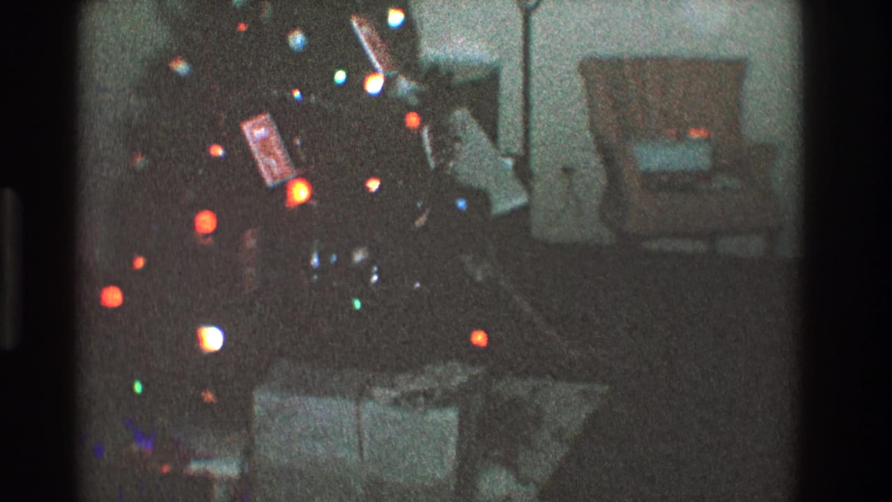 Dim living room with a lit Christmas tree, wrapped gifts, armchair, and floor lamp.