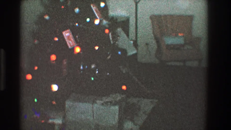 1968 Toledo 8mm frame showing a dim Christmas tree with colored lights, presents below, and a chair and lamp in the background.