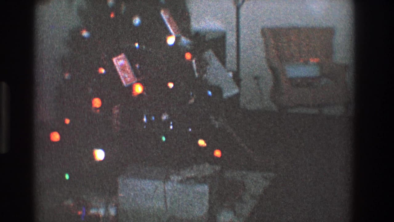 Lit Christmas tree beside presents, with an armchair and lamp in the dim background.