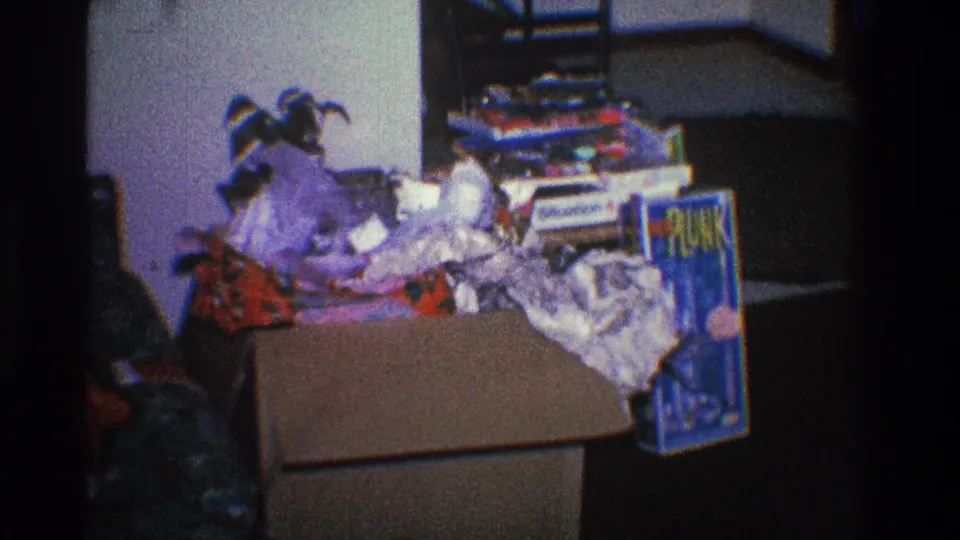 A soft-focus 1968 Toledo frame shows post-gift clutter, including an open cardboard box, wrinkled paper, packages, and a small jester-style hat.