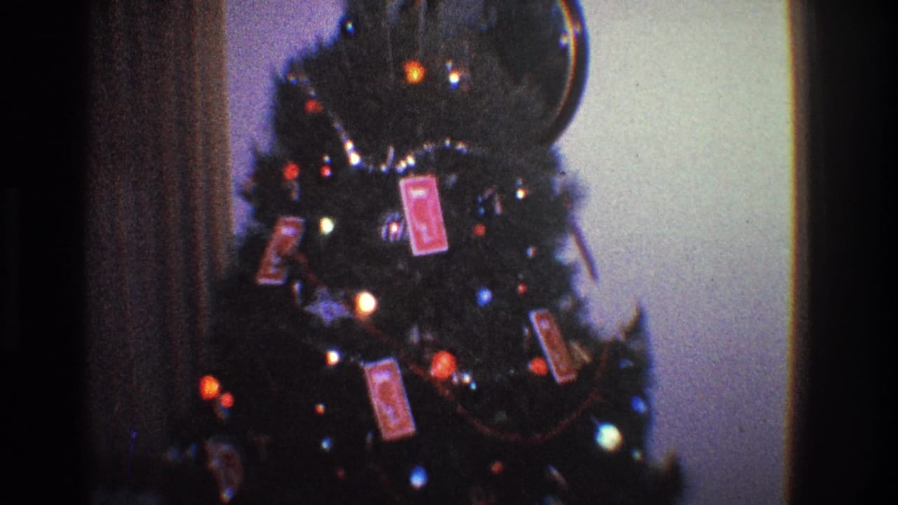 Decorated Christmas tree with colored lights and red playing card ornaments in a dim room.