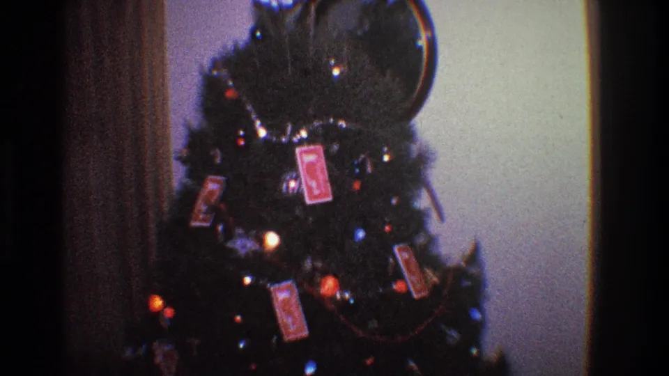 1968 Toledo home-movie view of a Christmas tree with colored lights and red card ornaments in a private interior.