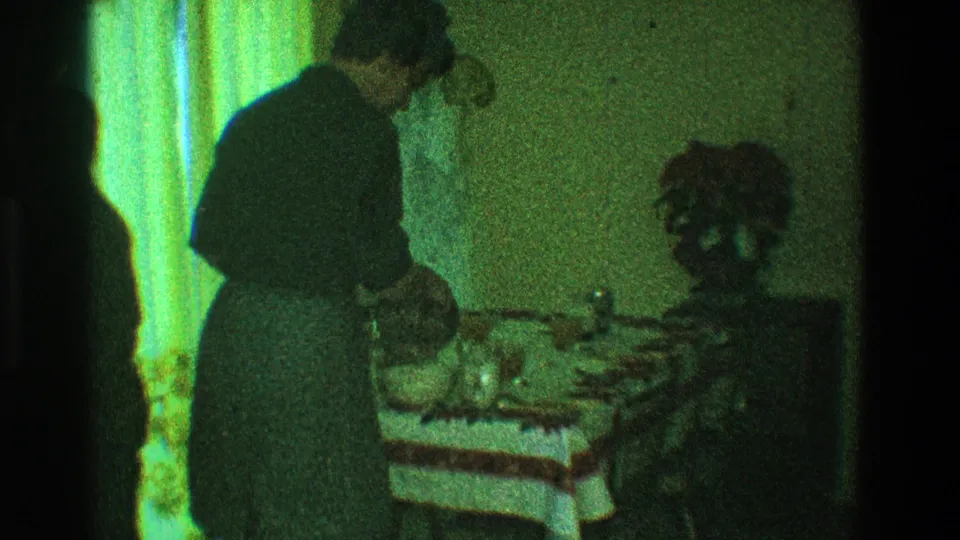 1968 Toledo interior frame showing a woman preparing food at a table, with a green-tinted curtain and table setting nearby.
