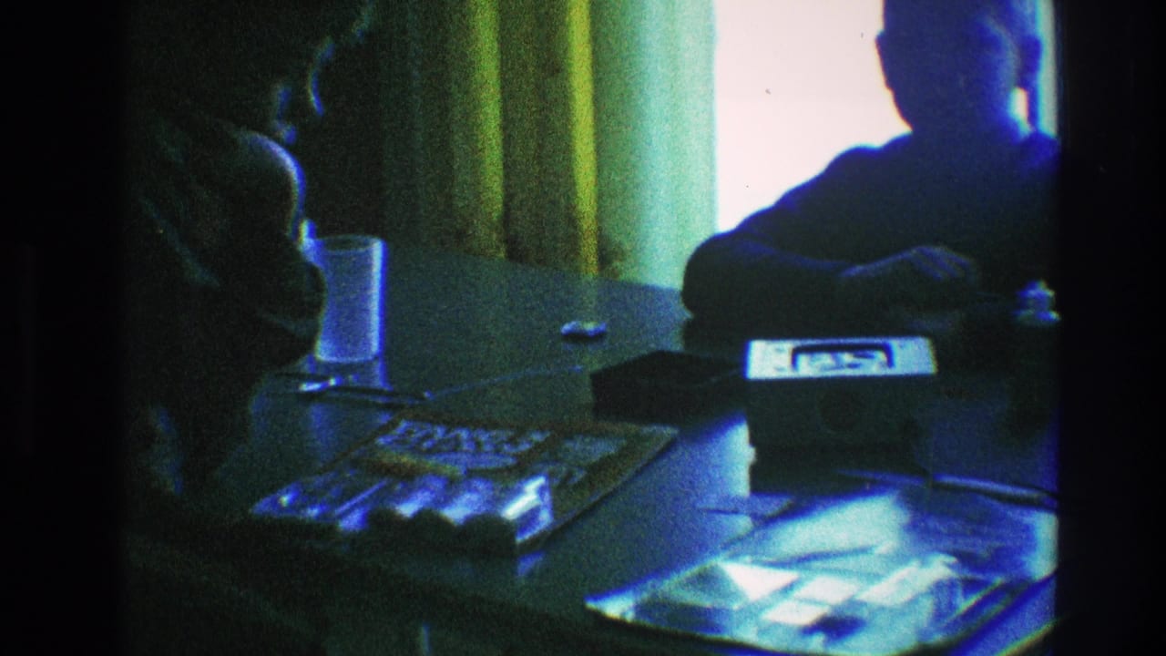 A dim 1968 Toledo interior shows a seated figure at a reflective table with a glass, papers, and window curtains.