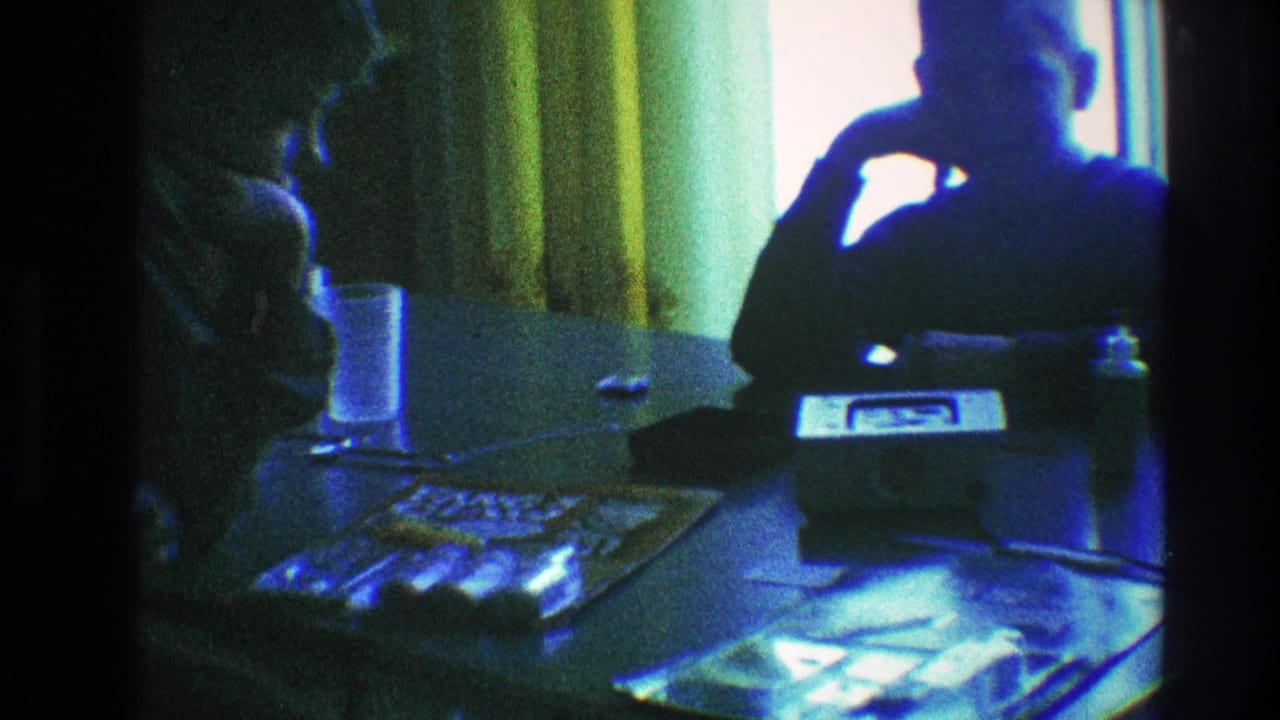 A silhouetted person rests an arm near the face while another figure sits in profile beside a table.