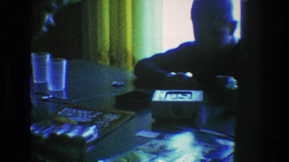 The boy sits behind the small radio in the Toledo home interior, with papers and glasses on the table and strong blue-green 8mm color cast.