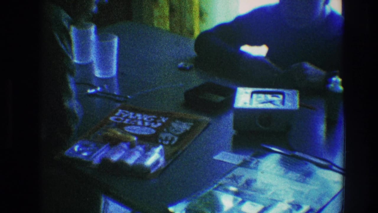 1968 Toledo home-movie frame showing a Green Hornet comic and toy package on a brown table with glasses, a small device, and partial hands.