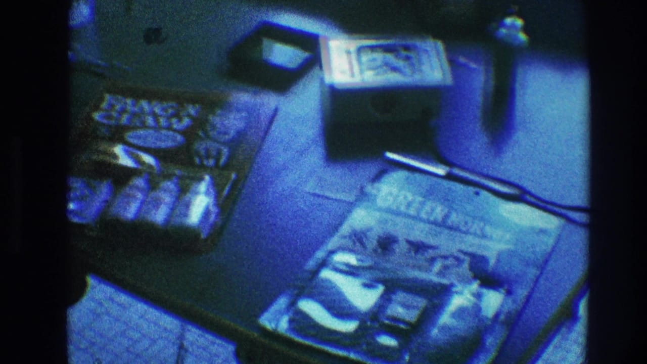 Tabletop view of a comic book, toy package, small device, cord, and drinking glasses in blue light.