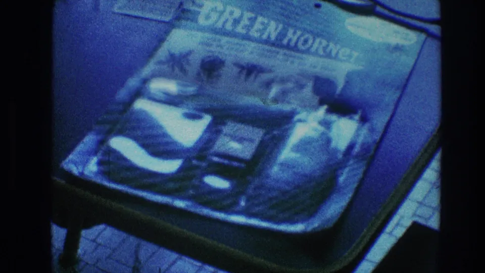 Close 8mm frame from 1968 Toledo centered on a Green Hornet comic book lying on a table, with a cord and table edge visible.