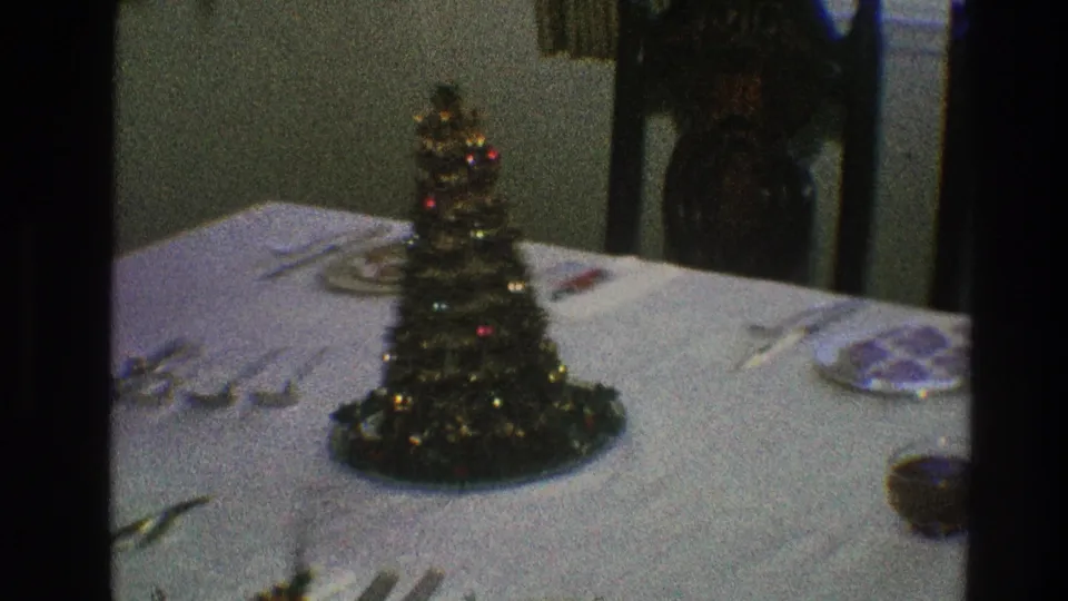 1968 Toledo frame of a prepared Christmas Eve table with a small decorated tree, white cloth, plates, utensils, and glassware visible.