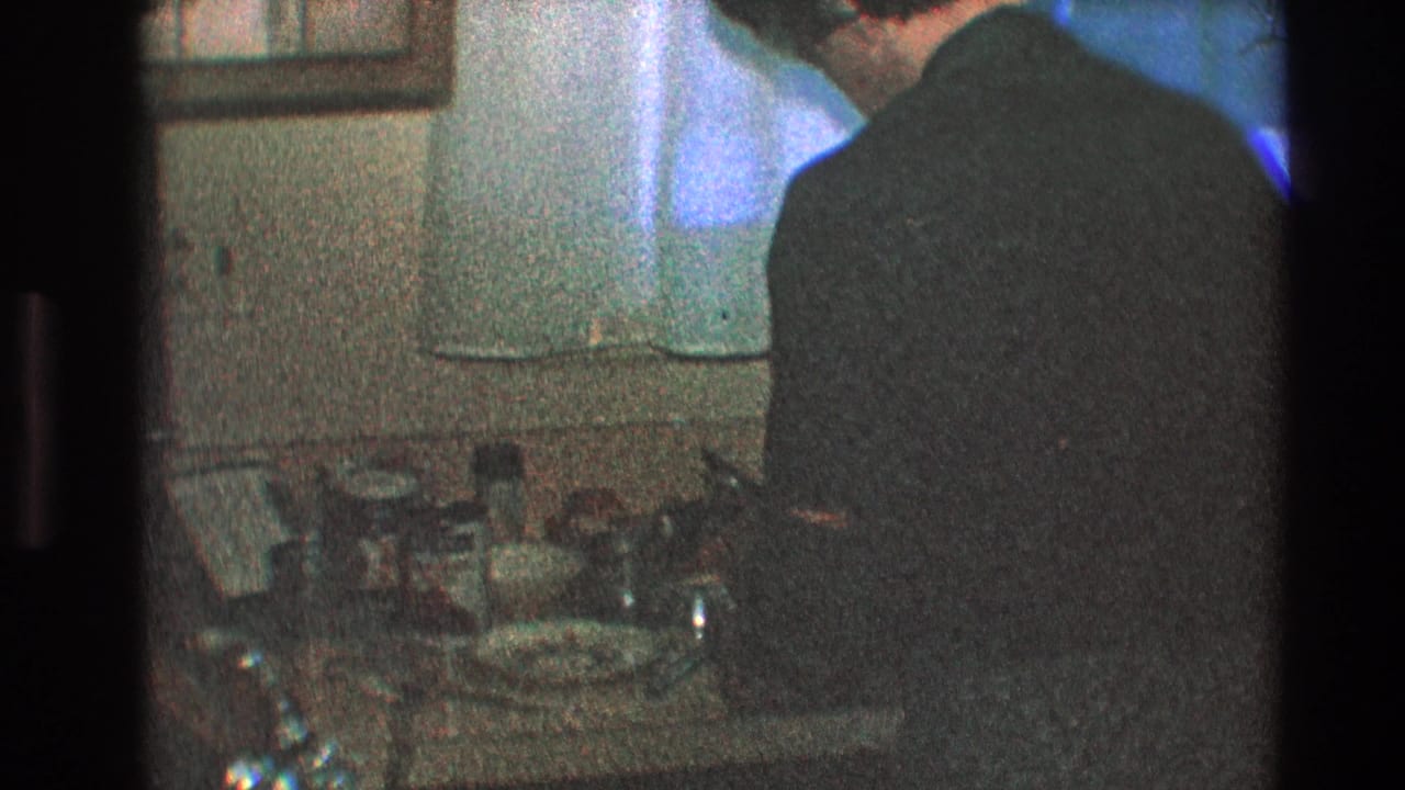 In a 1968 Toledo home interior, a man in a dark sweater stands at a kitchen counter beneath white curtains.