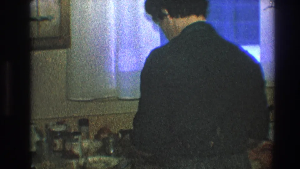 In this 1968 Toledo home-movie frame, a man in a dark sweater stands with his back to the camera at a kitchen sink.