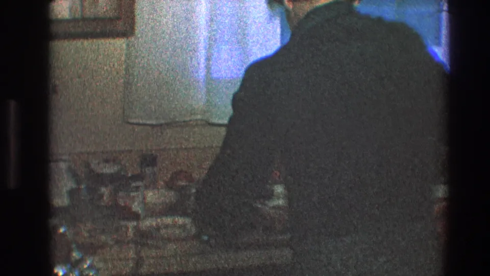 The 8mm frame shows the man leaning forward at the sink in a dim Toledo kitchen, surrounded by dishes and household items.