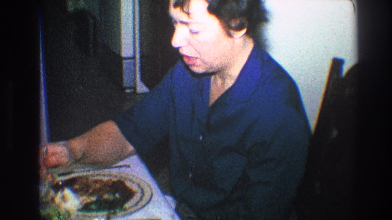Older woman in a blue shirt eats at a table with a plate of food.