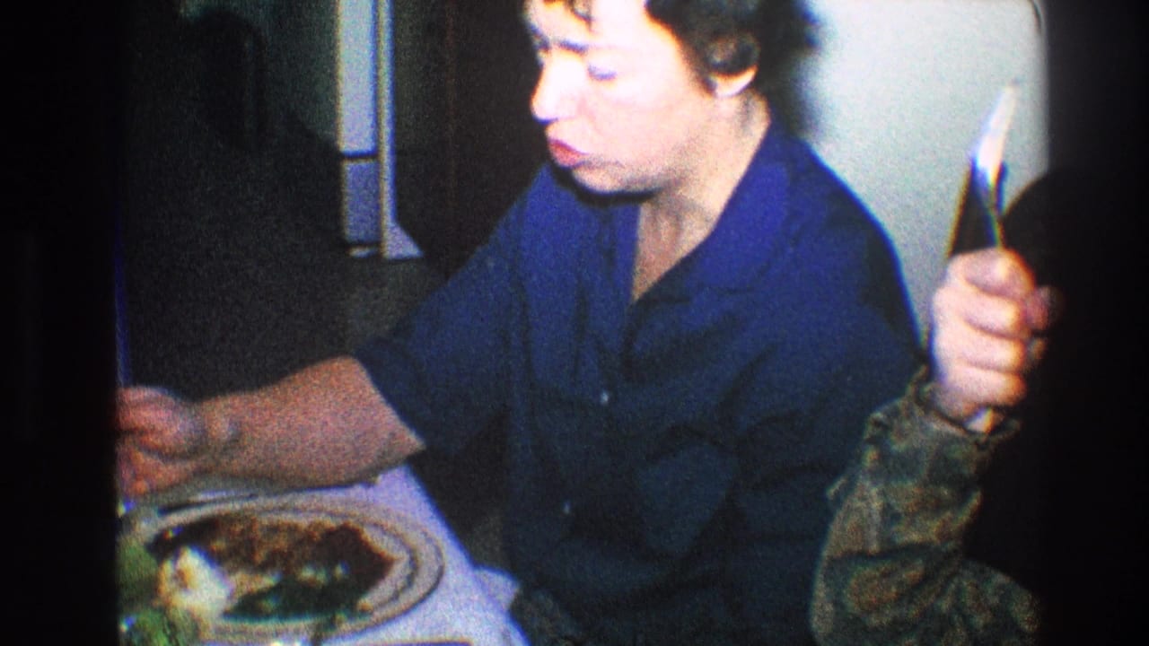 Older woman sits at a table while a hand appears near her shoulder.