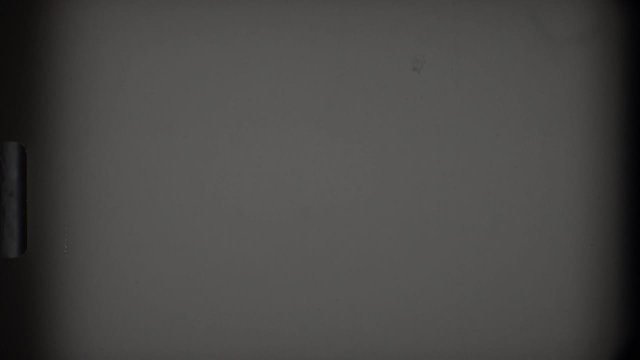 Dark, partial frame showing pale wall or cabinet surfaces with film edge shadows.