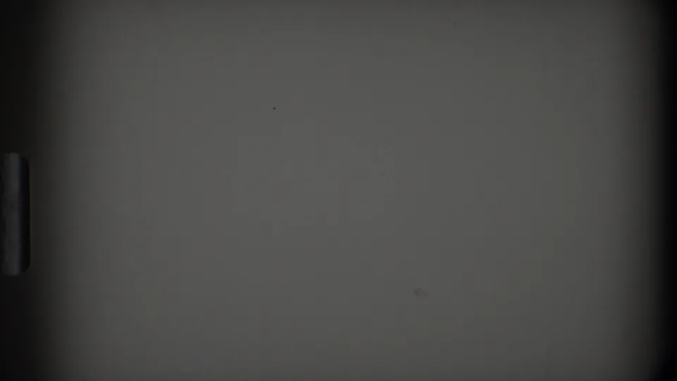 Low-light 8mm frame from the 1968 Toledo home movie showing a plain interior surface and a narrow vertical fixture.